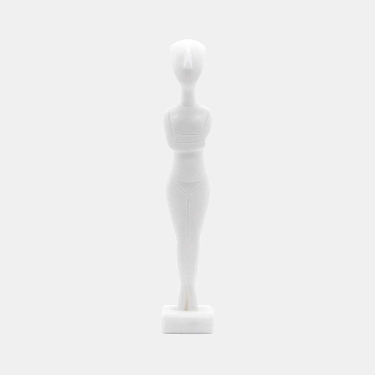 The image shows a stylised white statue or figurine made from White Naxos Marble. It is a simplified representation of a human figure with an abstract and geometric design. The figure has no facial features and stands upright on a small base. The aesthetic is minimalist, focusing on form and shape rather than detail.