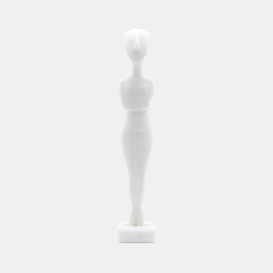 The image shows a stylised white statue or figurine made from White Naxos Marble. It is a simplified representation of a human figure with an abstract and geometric design. The figure has no facial features and stands upright on a small base. The aesthetic is minimalist, focusing on form and shape rather than detail.