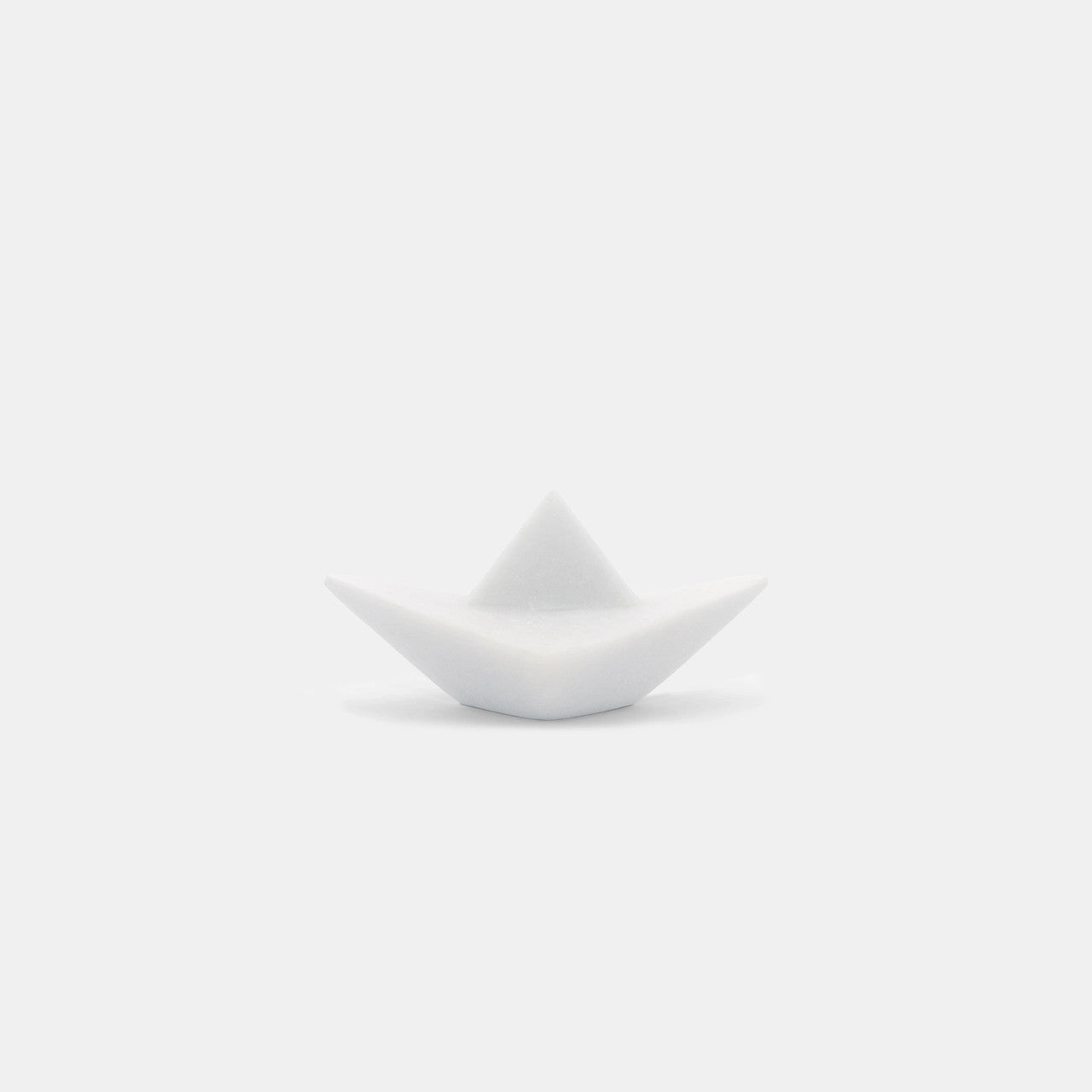 The photograph portrays an elegant sculpture of an origami paper boat, expertly crafted from pristine Naxos Marble. This minimalist piece, with its fold-like design suggestive of a boat, is displayed against a pure white backdrop.