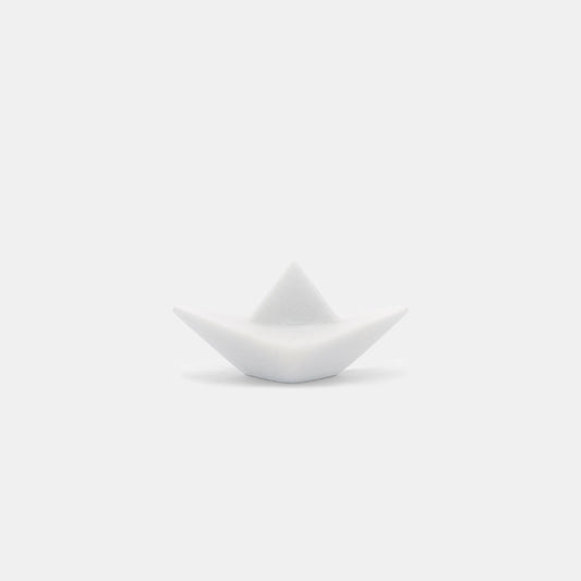 The photograph portrays an elegant sculpture of an origami paper boat, expertly crafted from pristine Naxos Marble. This minimalist piece, with its fold-like design suggestive of a boat, is displayed against a pure white backdrop.
