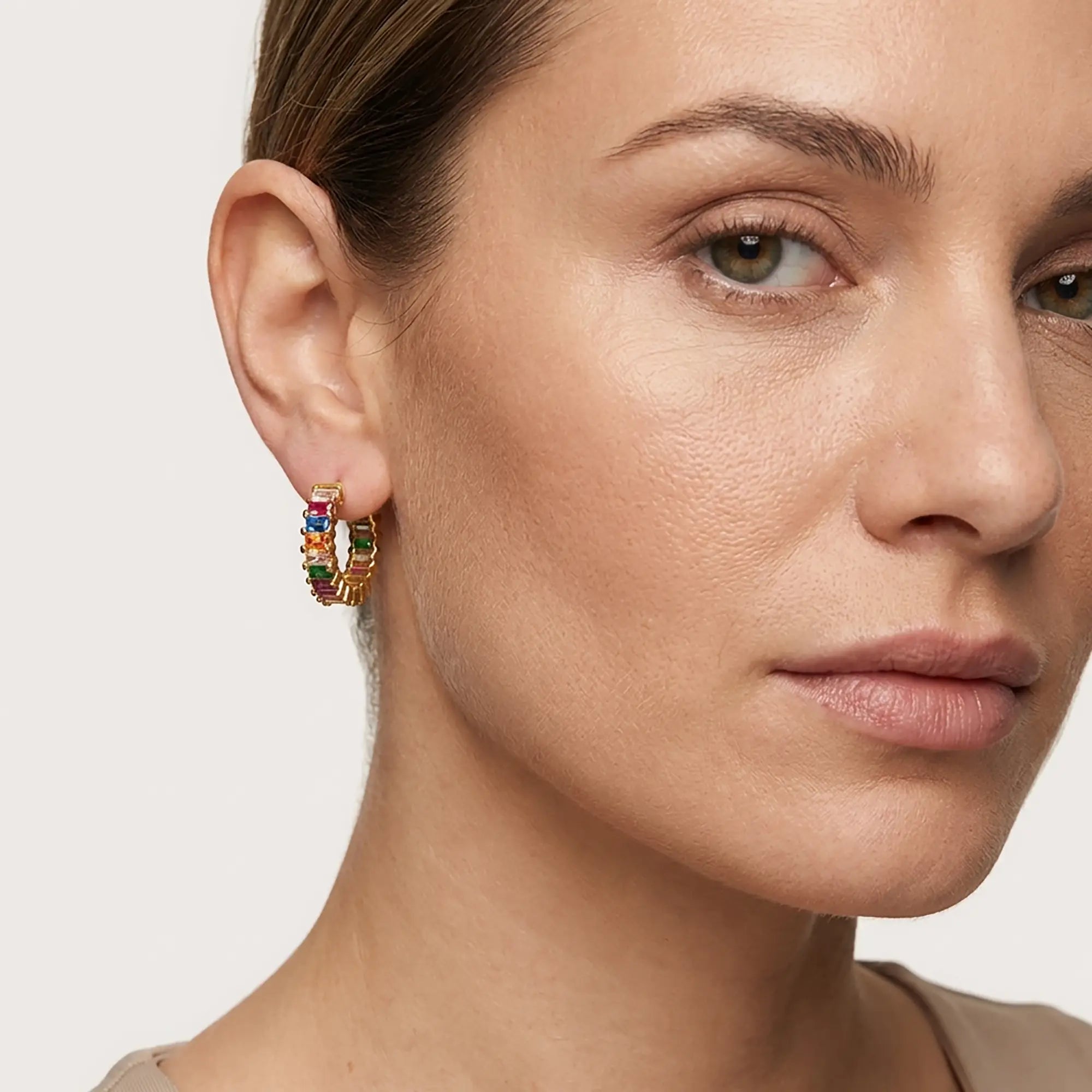Close-up of a woman wearing colorful hoop earrings with a neutral background