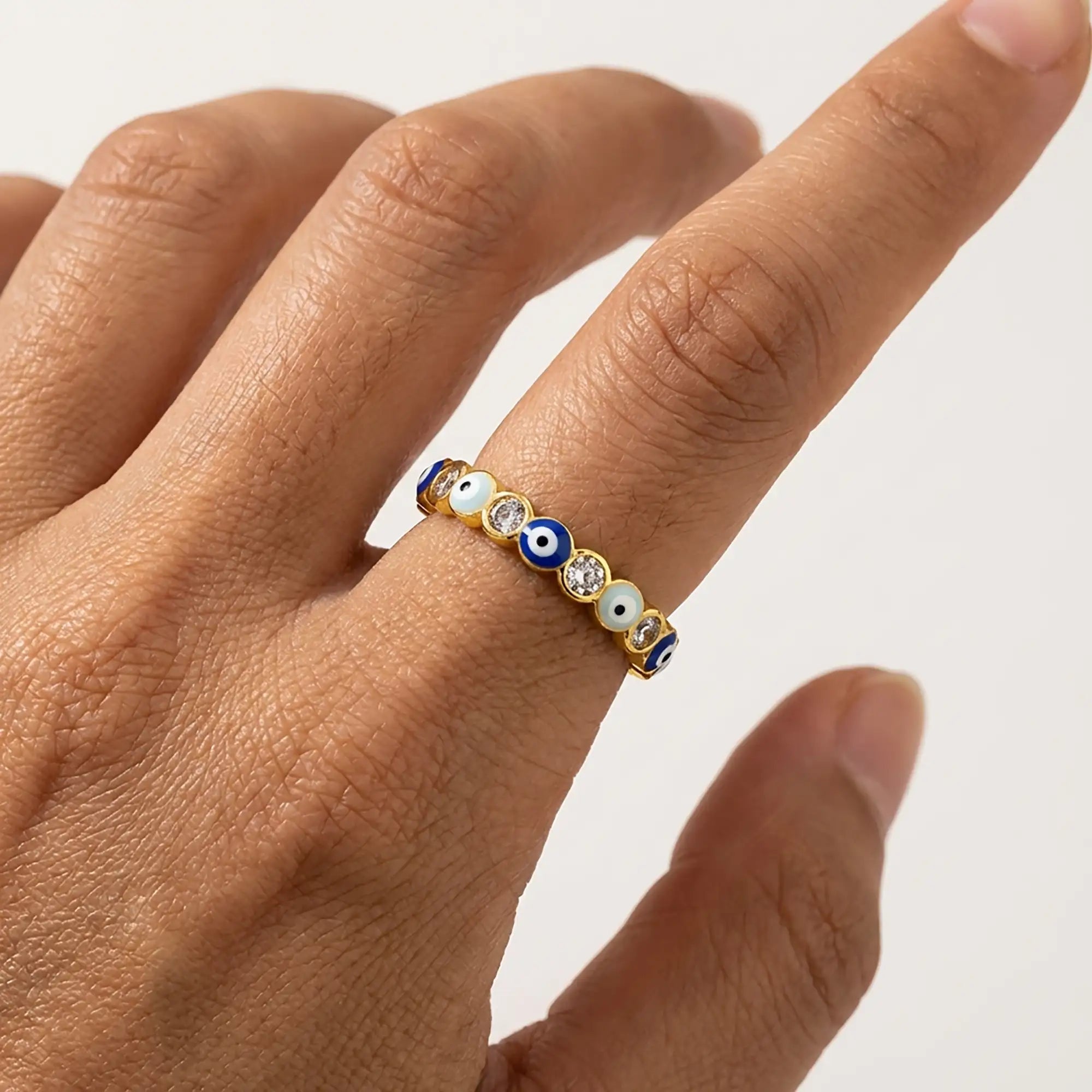 Closeup of an adjustable gold evil eye ring with blue enamel eye details and clear crystals worn on a hand