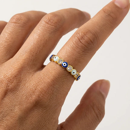 Closeup of an adjustable gold evil eye ring with blue enamel eye details and clear crystals worn on a hand