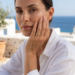 Woman wearing an adjustable gold evil eye ring with blue enamel eyes and crystals in a sunlit Greek island setting