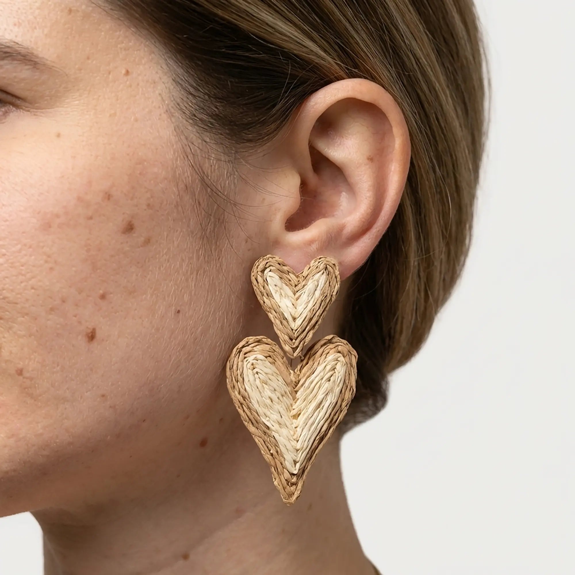 Woman wearing double heart woven statement earrings in a natural straw look