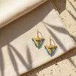 Medium blue fylachto earring on neutral fabric with gold plated sterling silver finish and blue accents