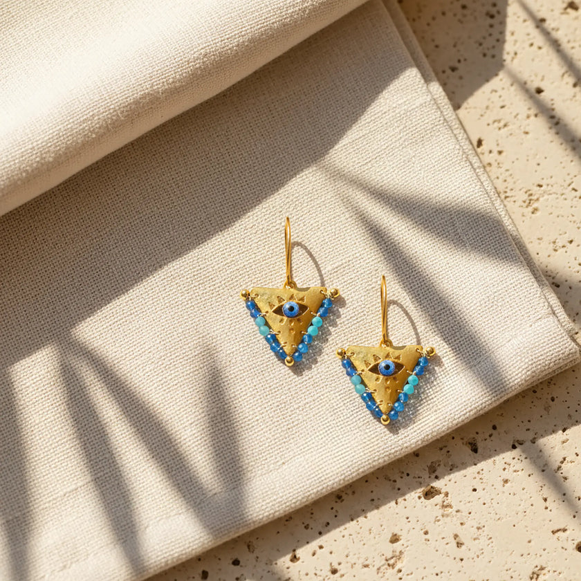 Medium blue fylachto earring on neutral fabric with gold plated sterling silver finish and blue accents