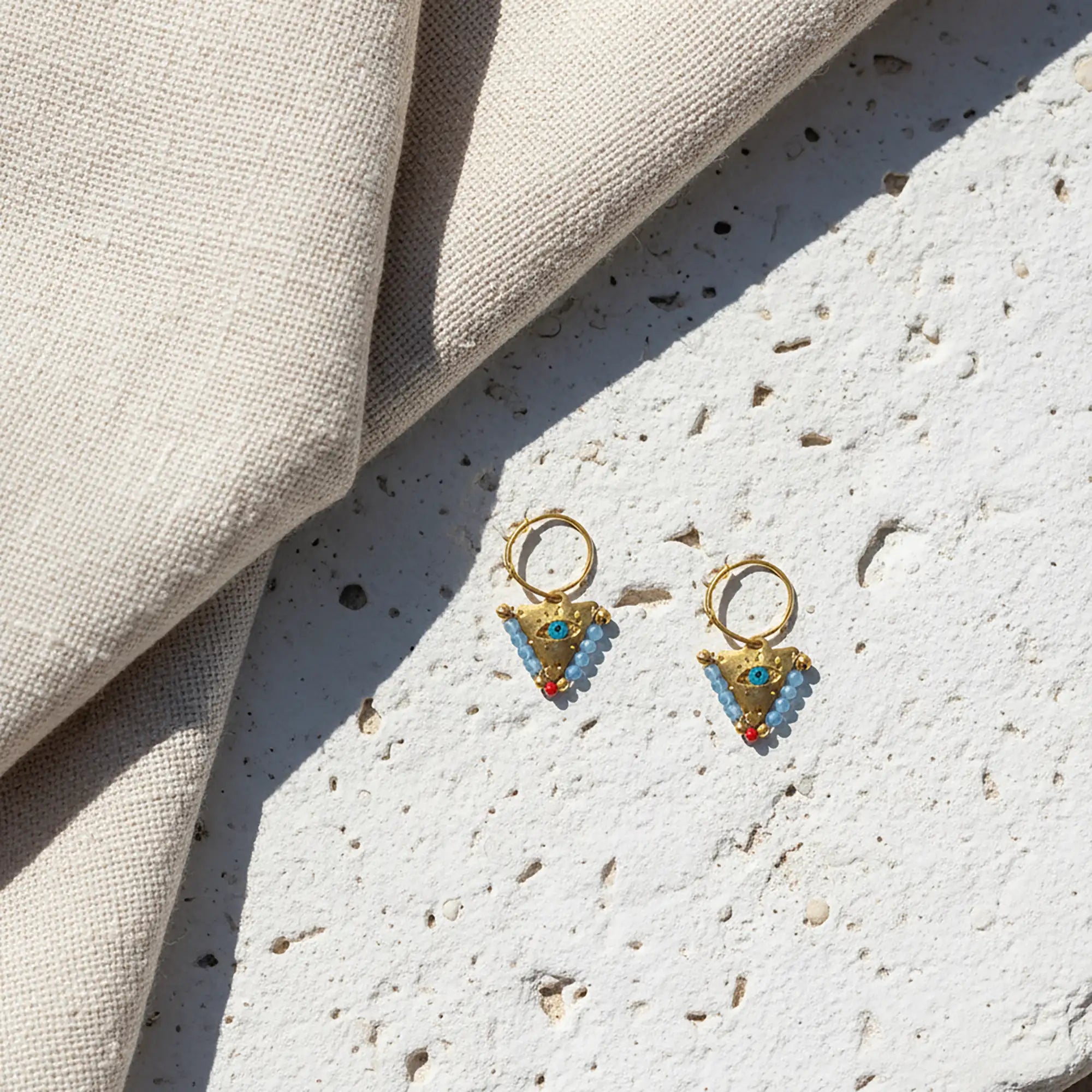 Small elephant gray and coral fylachto earring on neutral fabric with handpainted eye and bead details