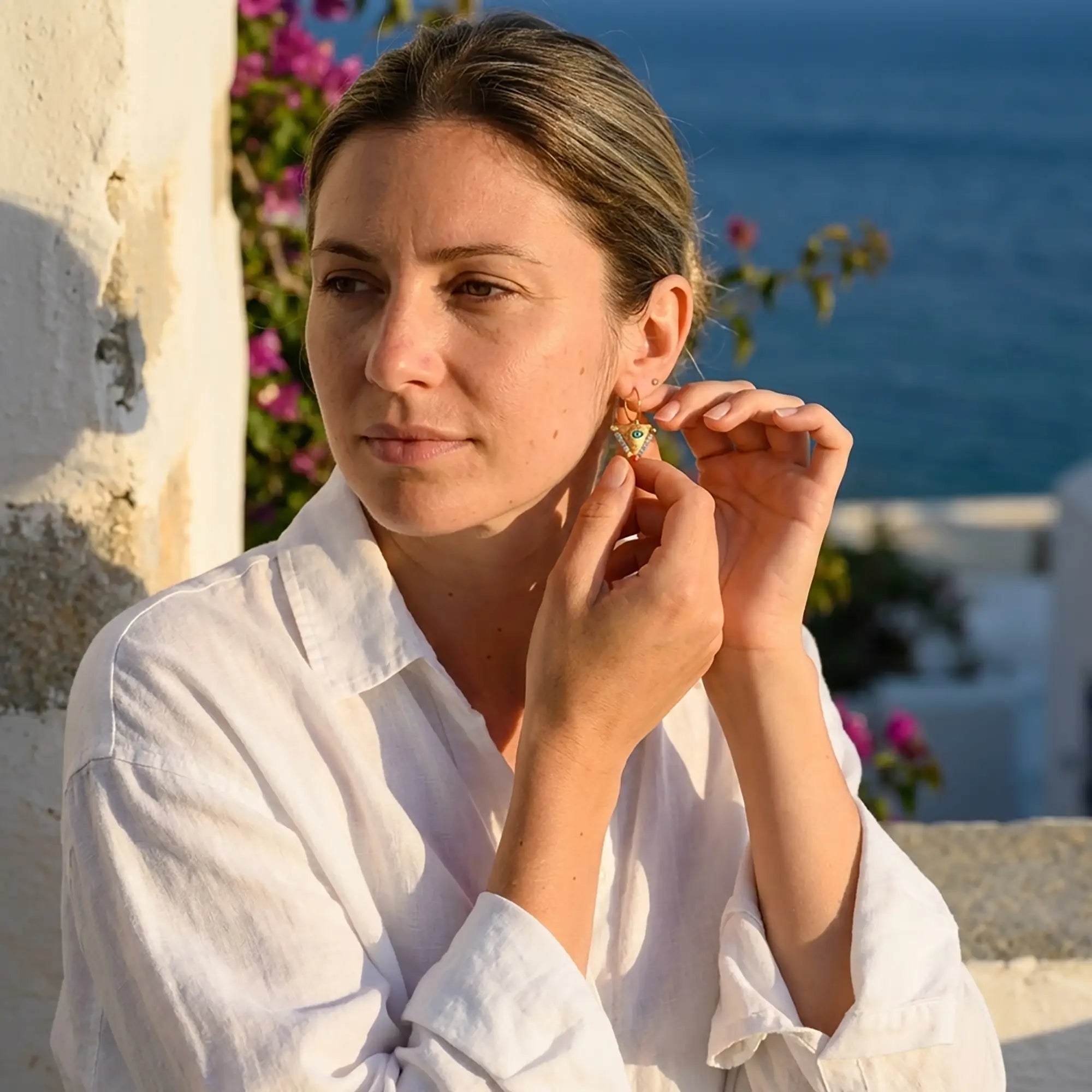 Woman wearing small elephant gray and coral fylachto earrings in gold plated sterling silver by the sea