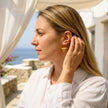 Woman wearing medium Sunset Reef fylachto earrings in gold plated sterling silver by the sea