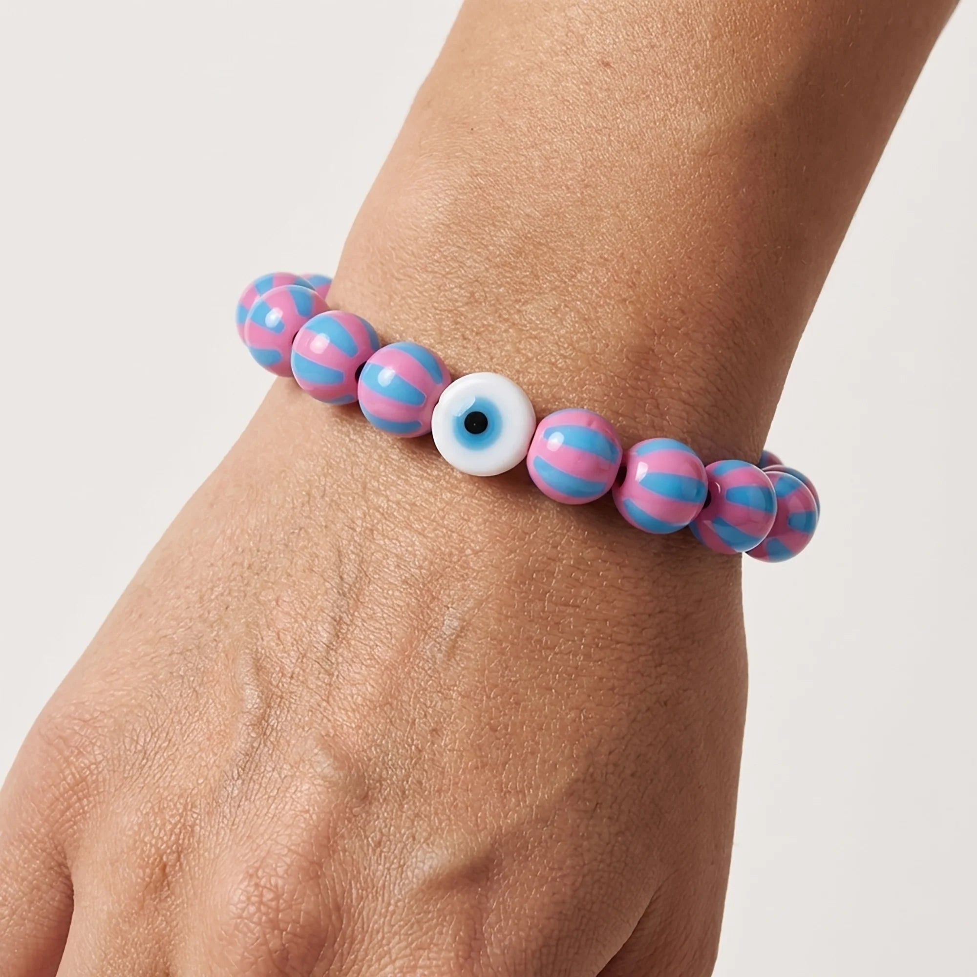 Woman wearing a handmade pink and blue striped bead bracelet with evil eye centerpiece