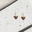 Pair of colorful small fylachto earrings with handpainted blue eye and purple coral bead details on light stone surface