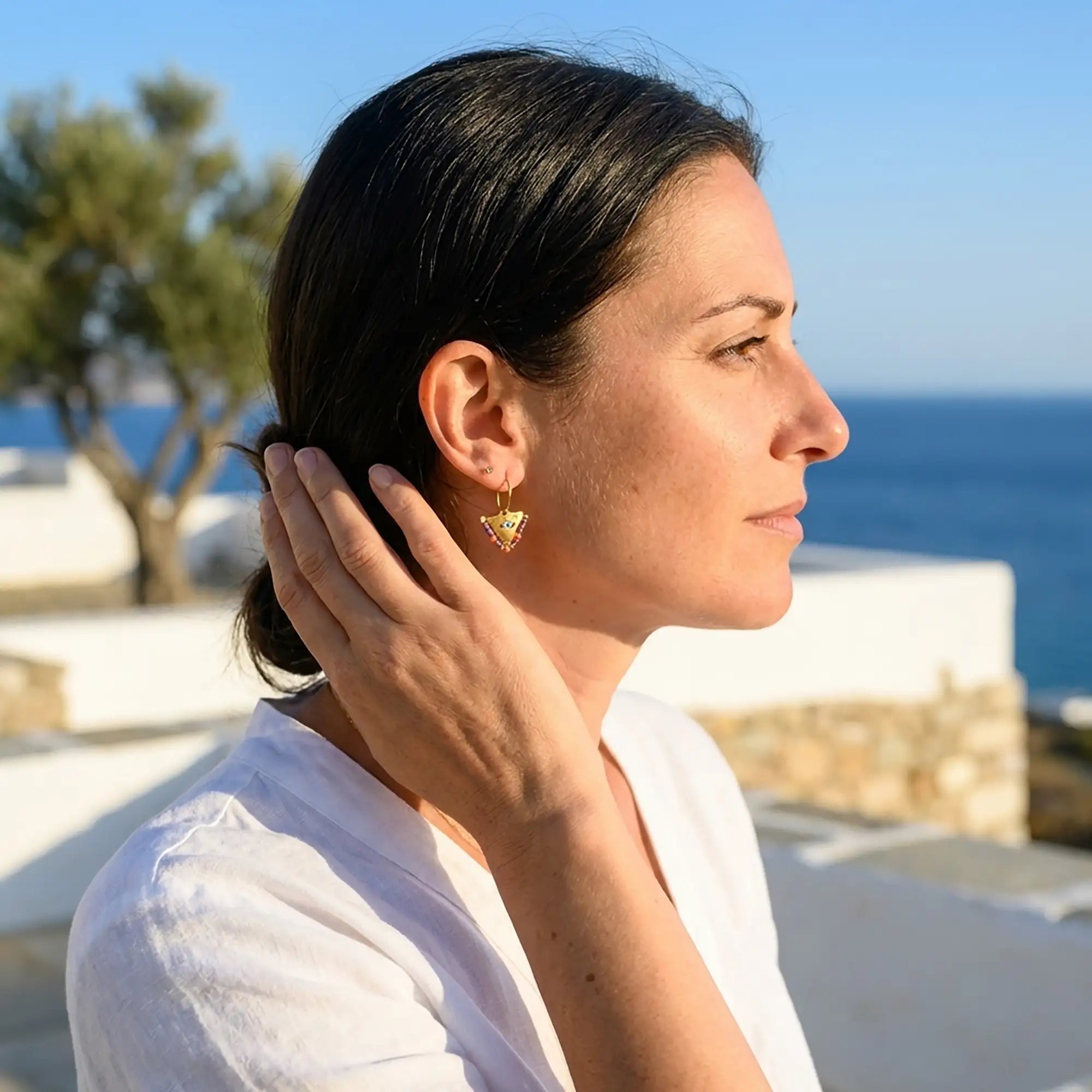 Woman wearing colorful small fylachto earrings inspired by Greek tradition in a sunlit Cycladic setting