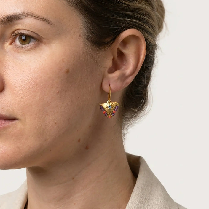 Woman wearing small colorful fylachto earrings in gold plated sterling silver with a handpainted blue eye