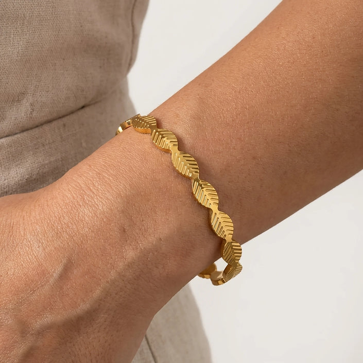 Woman wearing a gold tone stainless steel cuff bracelet with slim wave inspired design