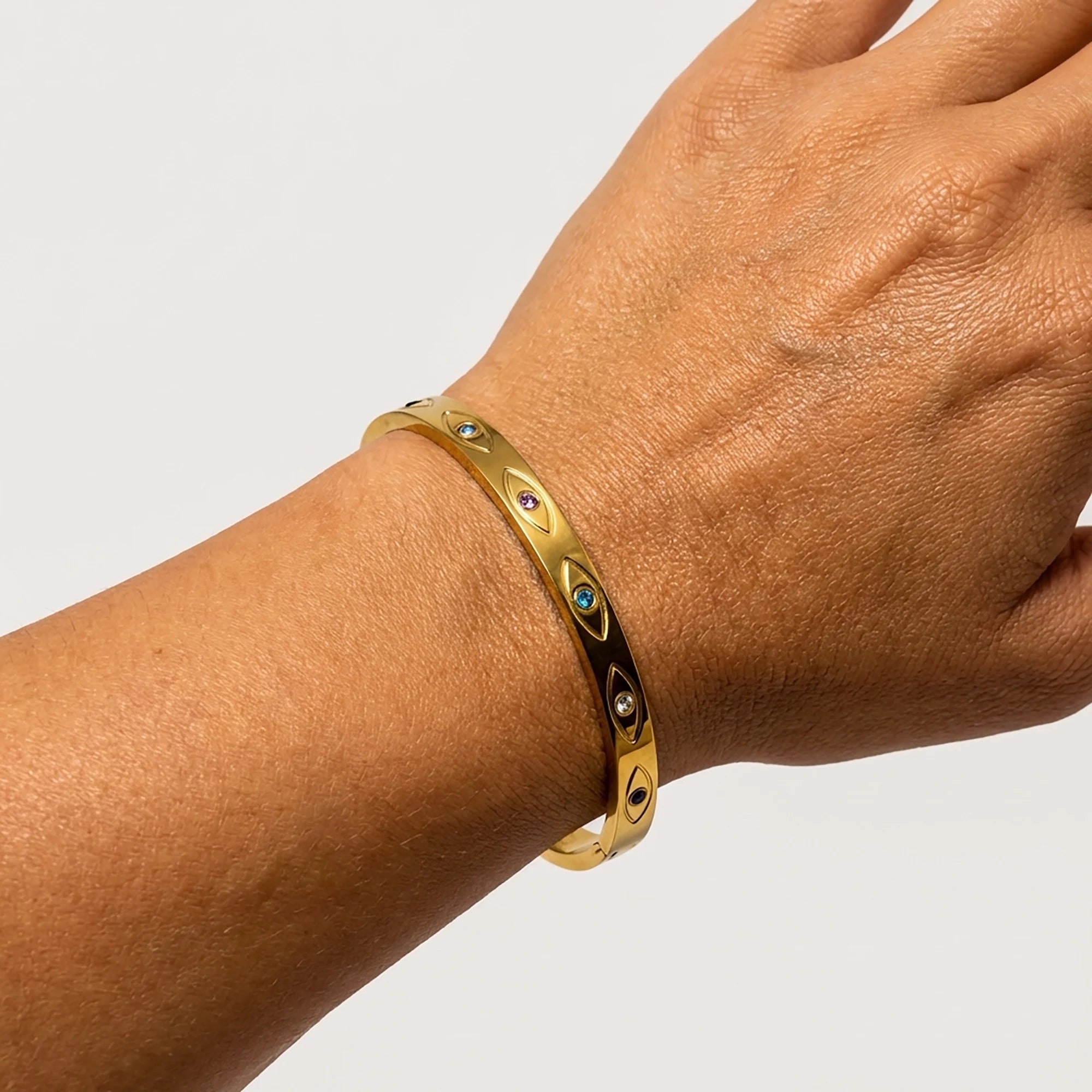 Woman wearing a gold tone stainless steel bangle bracelet with engraved evil eye motifs