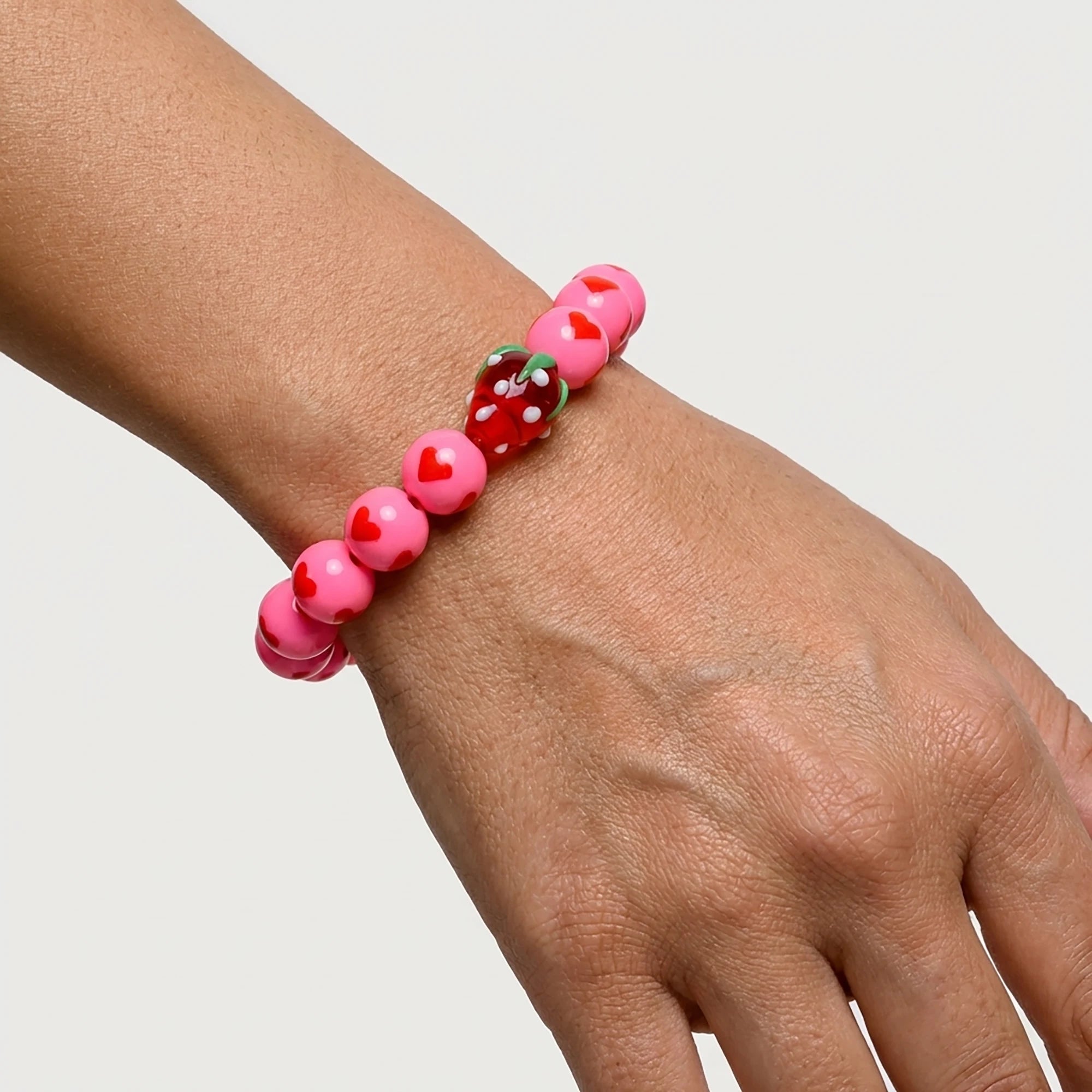 Woman wearing a handmade pink heart bracelet with Murano strawberry bead