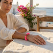 A woman wearing a pink bracelet on a stone surface with flowers in the background in Naxos, Greece