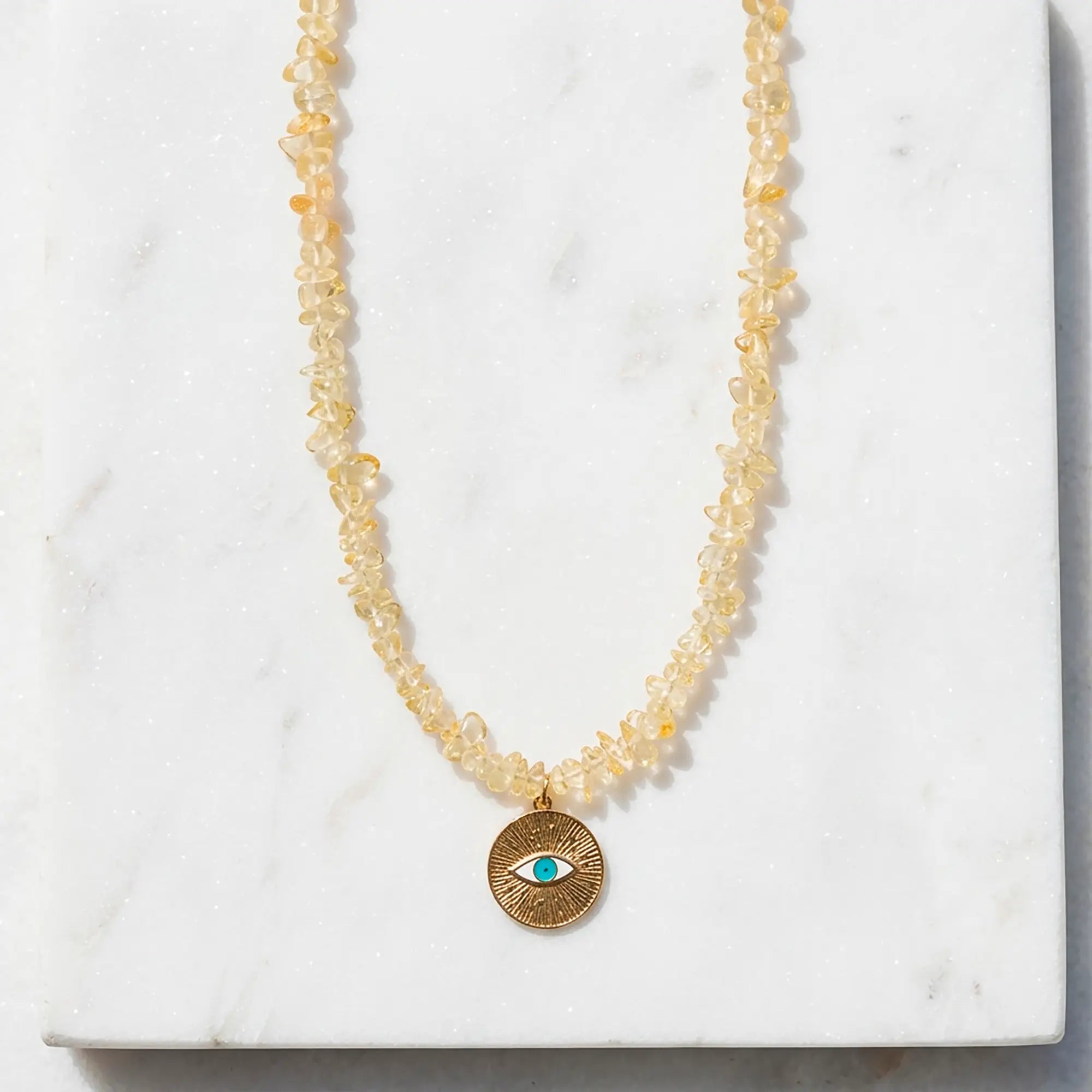Ilios citrine chip necklace with gold evil eye pendant styled on marble