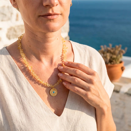 Ilios golden citrine necklace with evil eye pendant worn against Aegean sea