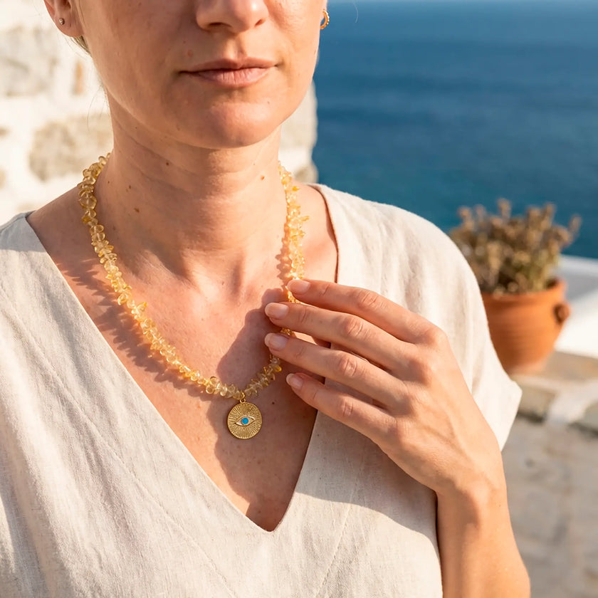 Ilios golden citrine necklace with evil eye pendant worn against Aegean sea