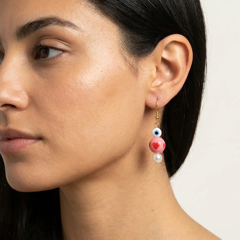 Close-up of pink heart and evil eye drop earrings with pearl detail