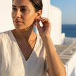 Woman wearing handmade pink heart pearl earrings with Greek evil eye detail in Naxos