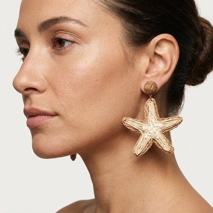 Woman wearing natural raffia starfish statement earrings in soft beige tones
