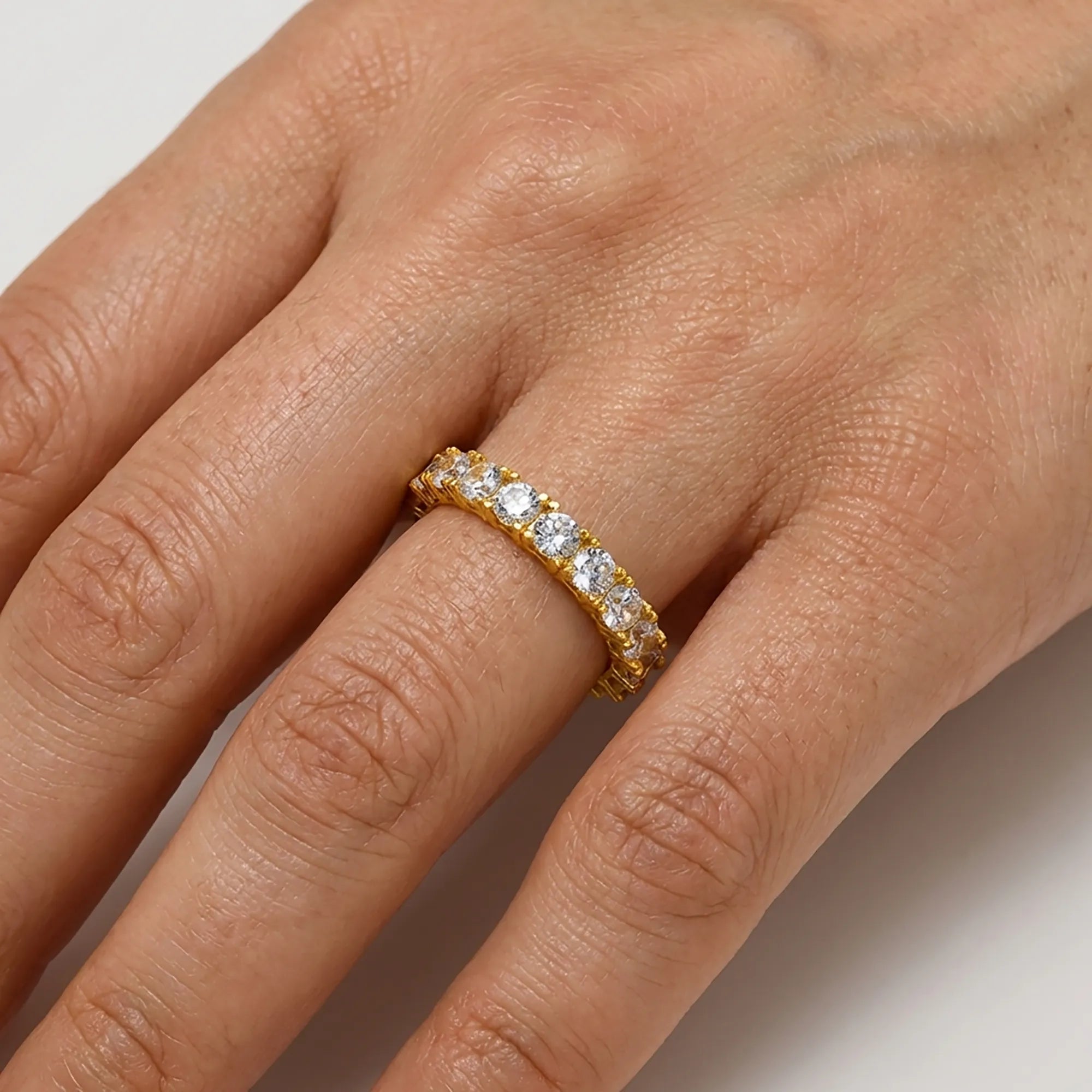 Gold ring with diamonds on a person's finger against a neutral background