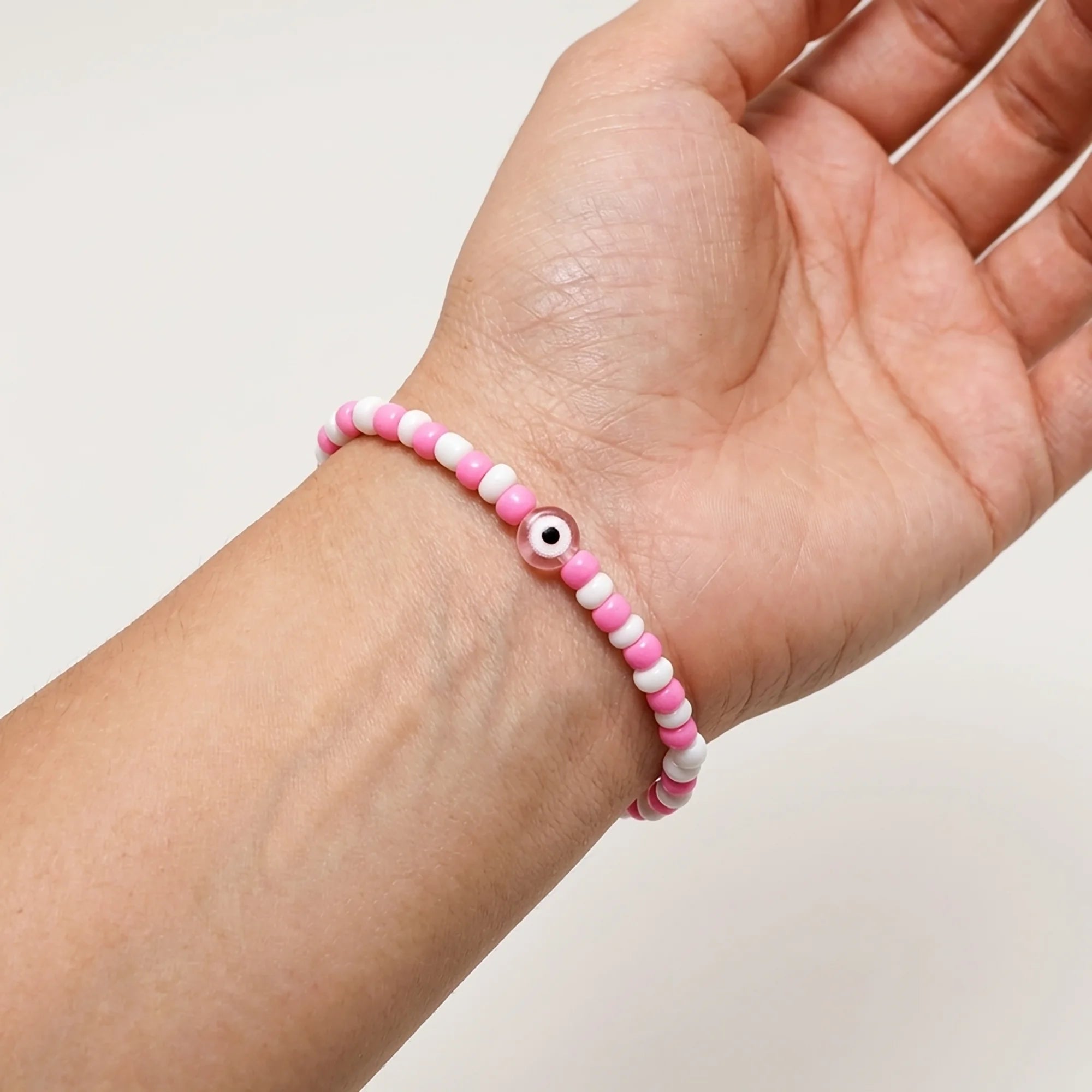Woman wearing a handmade pink and white bead bracelet with pink evil eye detail