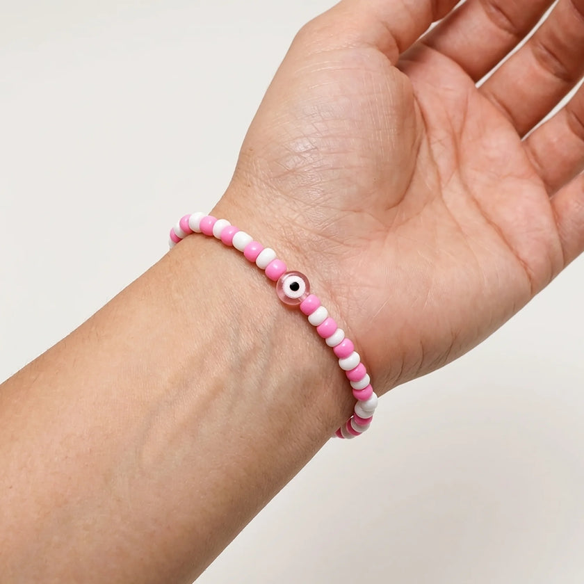 Woman wearing a handmade pink and white bead bracelet with pink evil eye detail