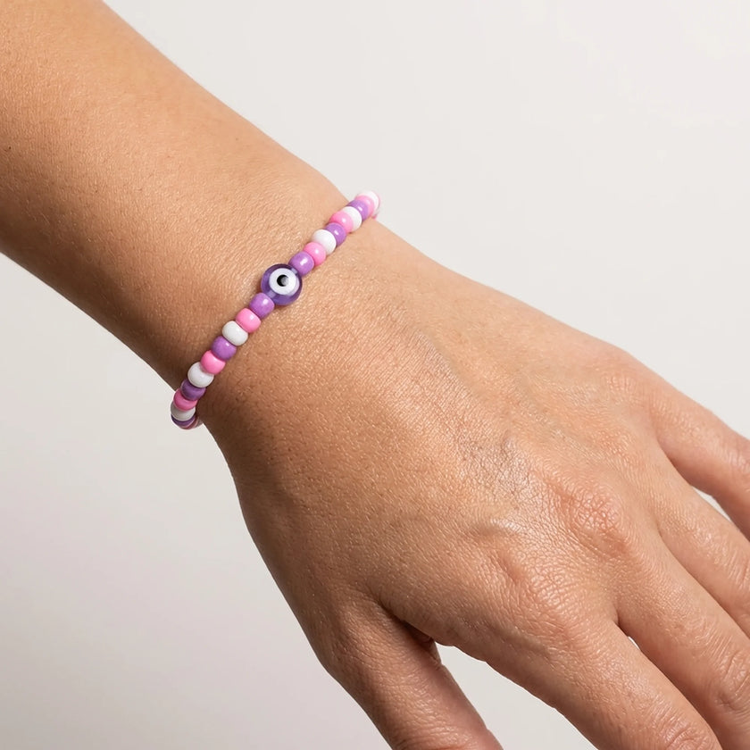 Woman wearing a pink and purple seed bead stretch bracelet with glass evil eye bead