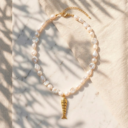 Freshwater pearl necklace with sculptural fish pendant styled on marble and linen