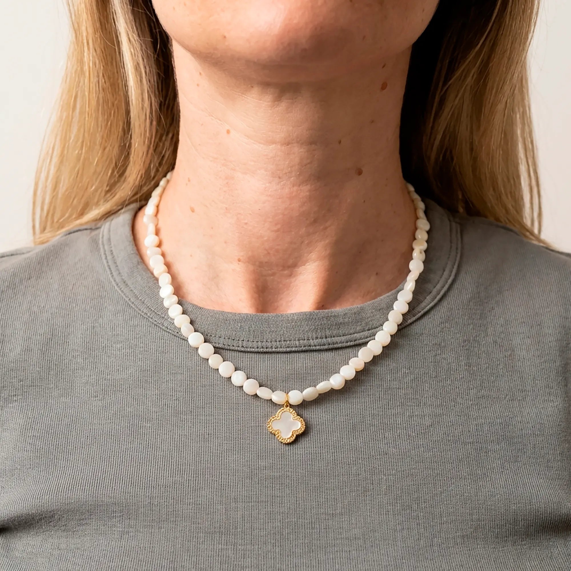 Selini pearl necklace with gold clover pendant worn with grey top