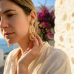 Woman wearing natural woven drop earrings in a sunlit Mediterranean setting