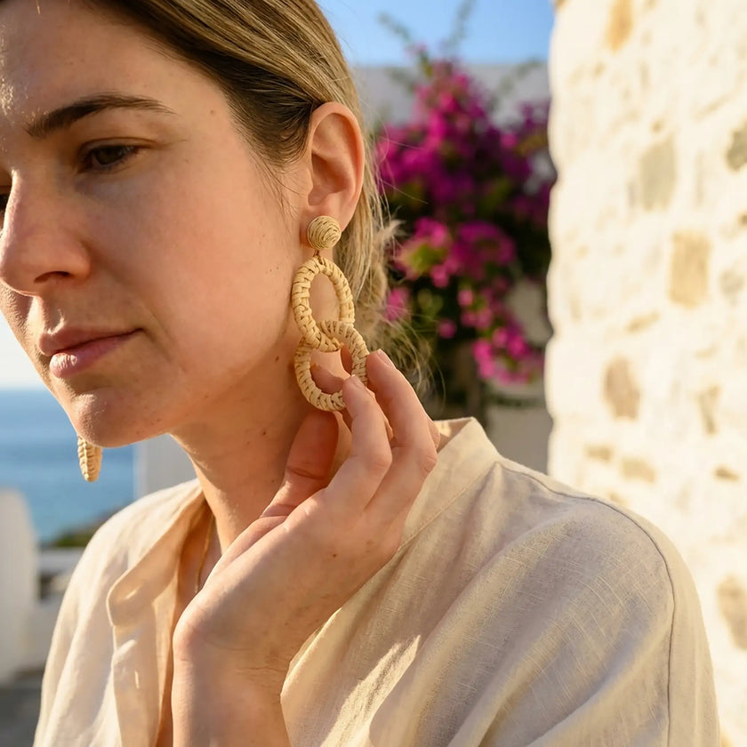 Woman wearing natural woven drop earrings in a sunlit Mediterranean setting