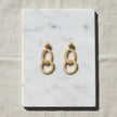 Natural woven double oval earrings displayed on white marble with soft neutral fabric